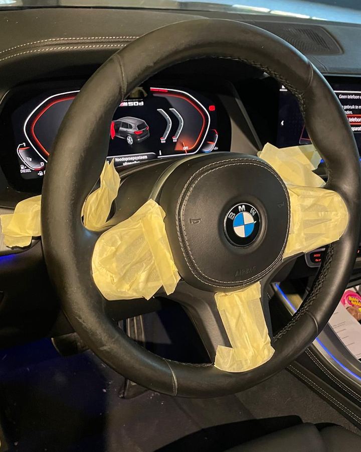 Stuurwiel van een BMW, met gele afplaktape over de airbag en de spaken, gezien vanaf de bestuurdersstoel.