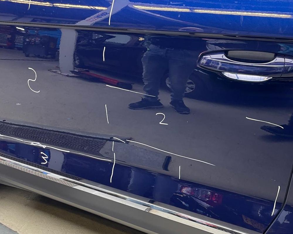 Donkerblauwe autodeur met met de hand geschreven witte cijfers en streepjes bij een aantal plekken op het paneel.