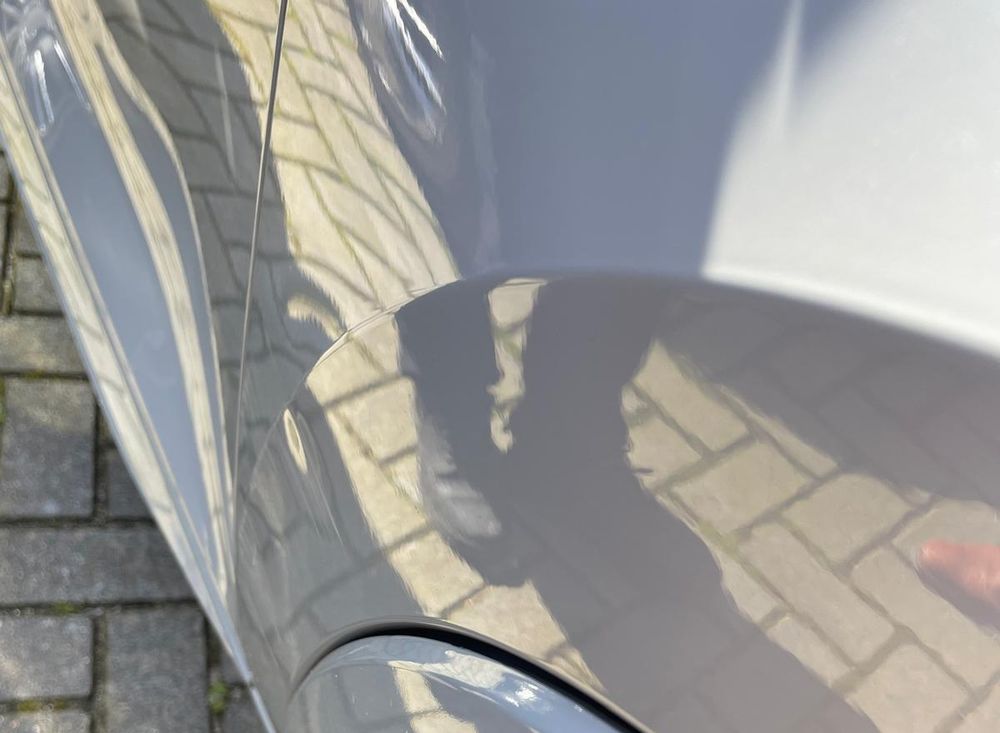 Zijkant van een grijze auto waarin de omgeving zich scherp en onvervormd in het spatbord weerspiegelt.